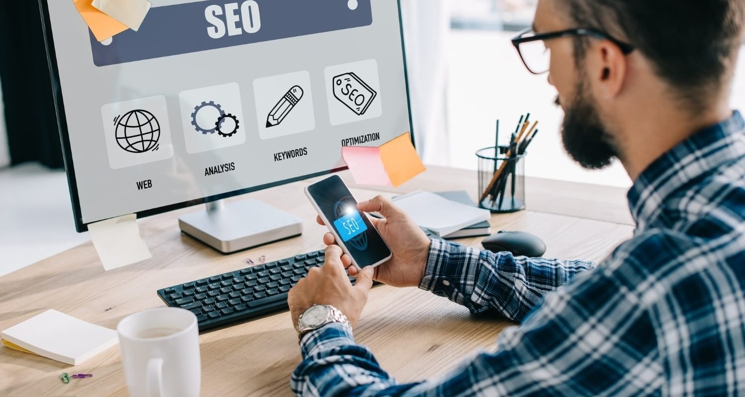 handsome-young-seo-manager-using-smartphone-and-computer-at-workplace-min.